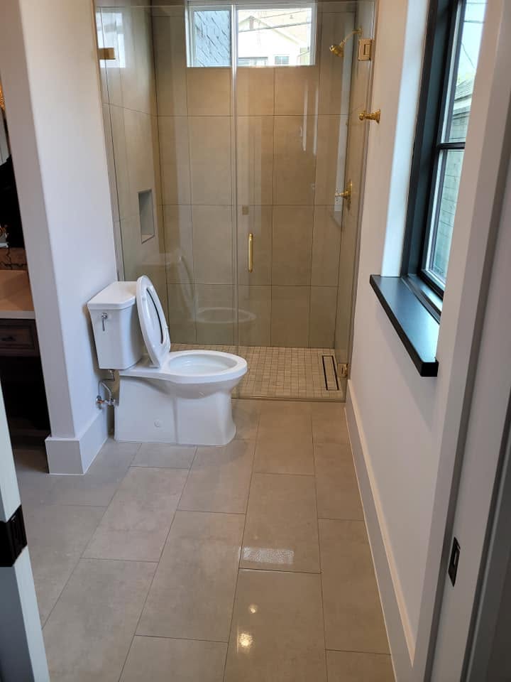 Modern bathroom with toilet, glass shower enclosure, and beige tile flooring