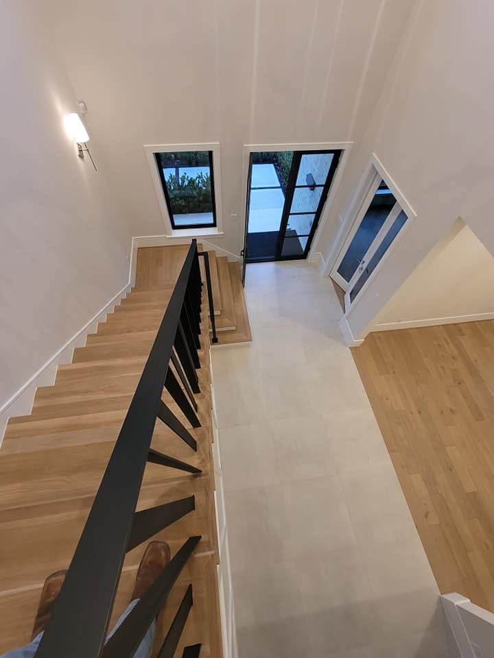 Modern staircase with black railing and wooden steps leading to bright upper floor with multiple windows