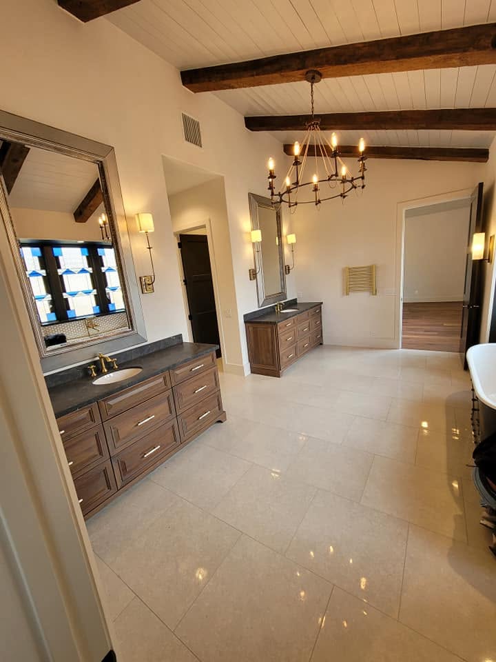 Spacious master bathroom with dual vanities, exposed beam ceiling, chandelier, and polished tile flooring