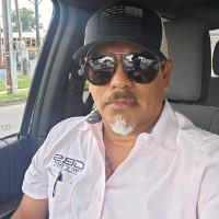 Man wearing white shirt, black cap, and sunglasses in vehicle