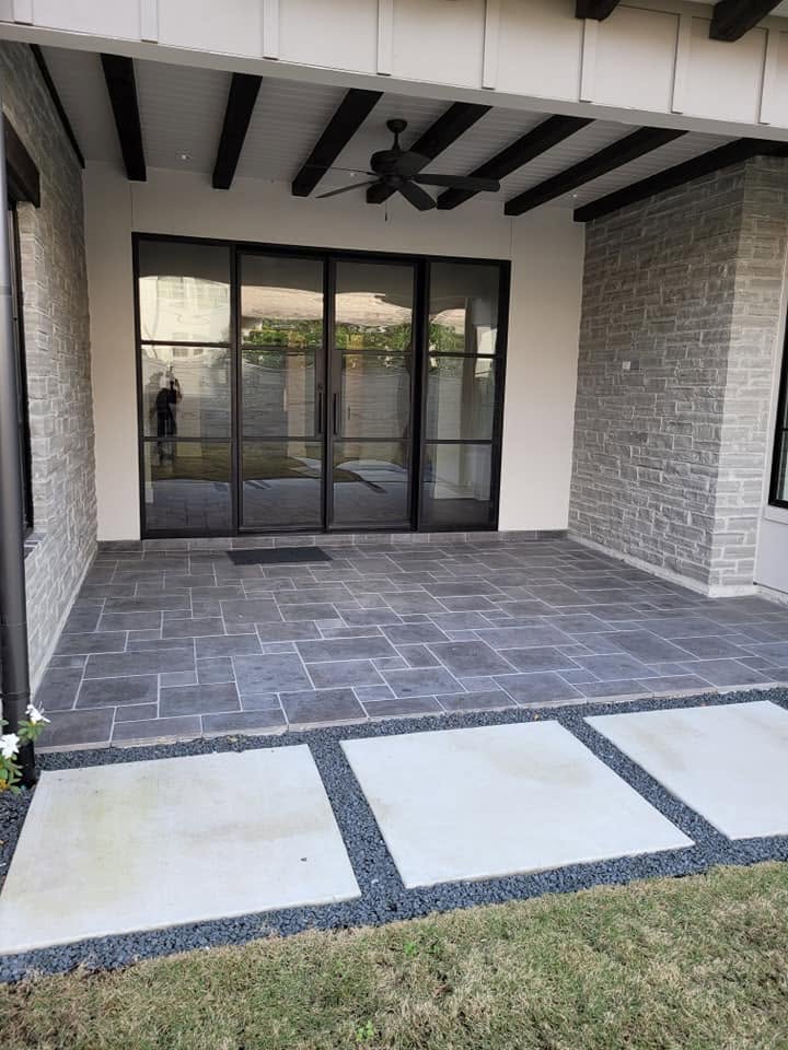 Modern covered patio with gray tile flooring, black framed glass doors, and brick walls