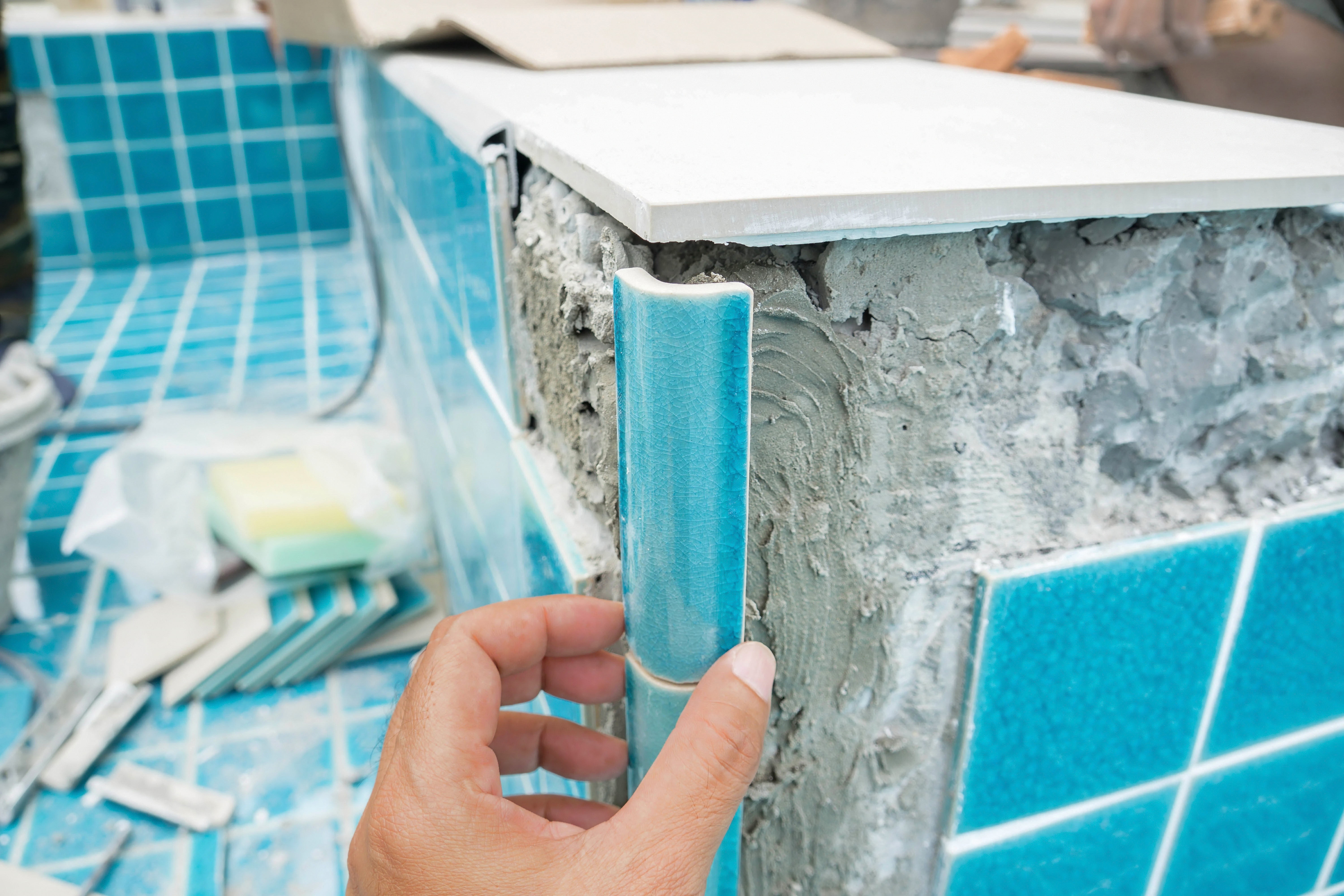 Hand holding blue pool edge trim tile against concrete pool structure
