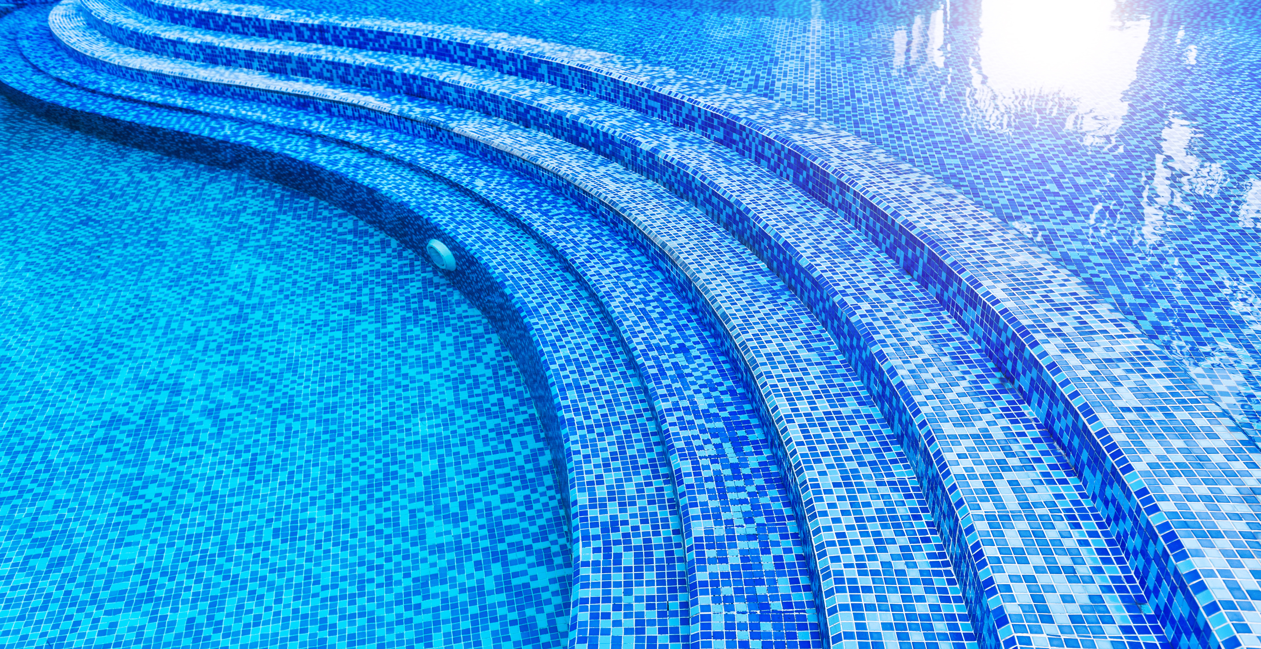 Swimming pool steps with blue mosaic tiles descending into clear water