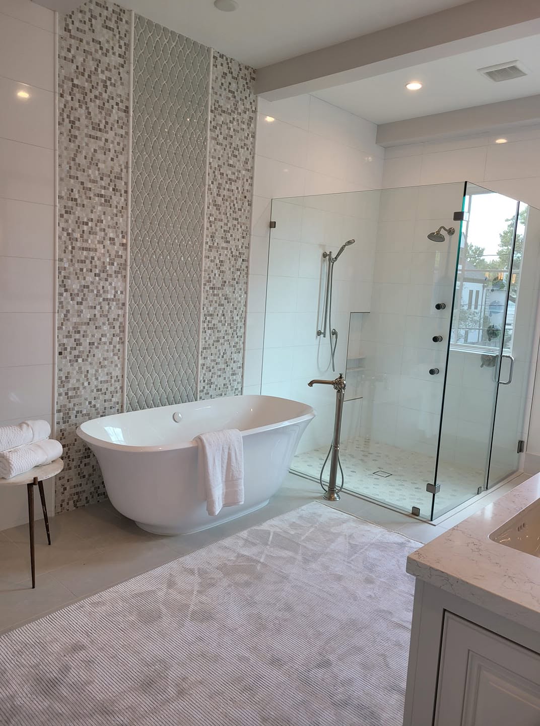 Modern spa bathroom with freestanding tub, glass shower enclosure, and decorative tile accent wall