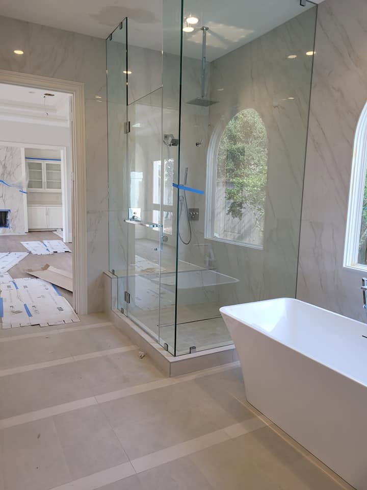 Modern bathroom with glass-enclosed shower, white soaking tub, and marble tile flooring under construction