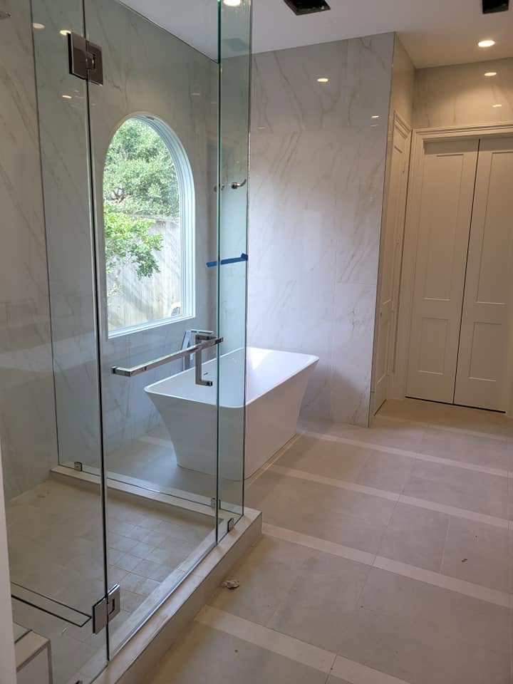 Modern bathroom with glass-enclosed shower, soaking tub, and arched window overlooking trees