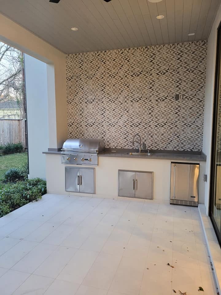 Modern outdoor kitchen with stainless steel grill, sink, refrigerator, and geometric tile backsplash